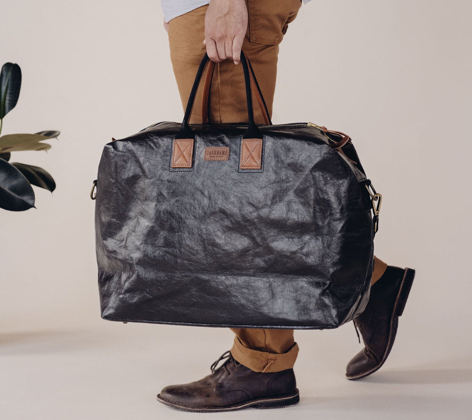 A man is carrying a large black washable paper holdall with brown leather details.