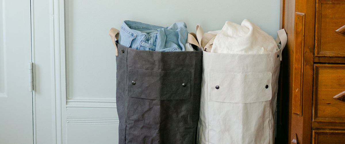 A grey and a white washable paper laundry bag hold denim and white washing. 
