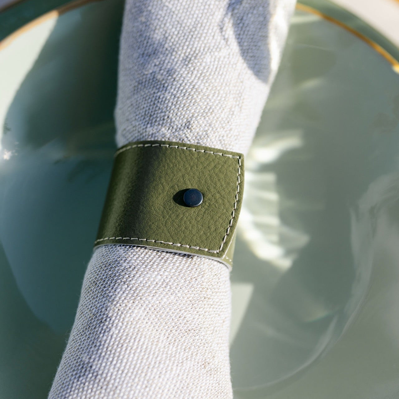 Napkin ring with a green band on a white napkin over a light blue plate.