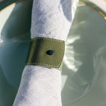 Napkin ring with a green band on a white napkin over a light blue plate.