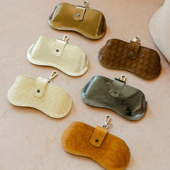 Six sunglasses cases in various colors on a beige surface