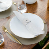 Table setting with white plates, gold cutlery, and a vase with greenery on a wooden table.