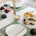 Dining table setting with plates, glasses, and bread basket on a green placemat.
