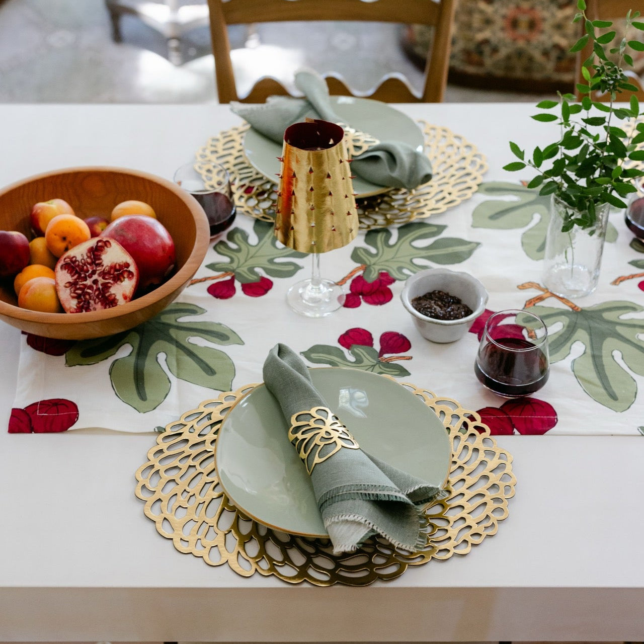 Dining table set with a floral tablecloth, gold chargers, and fruit bowl.