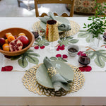 Dining table set with a floral tablecloth, gold chargers, and fruit bowl.