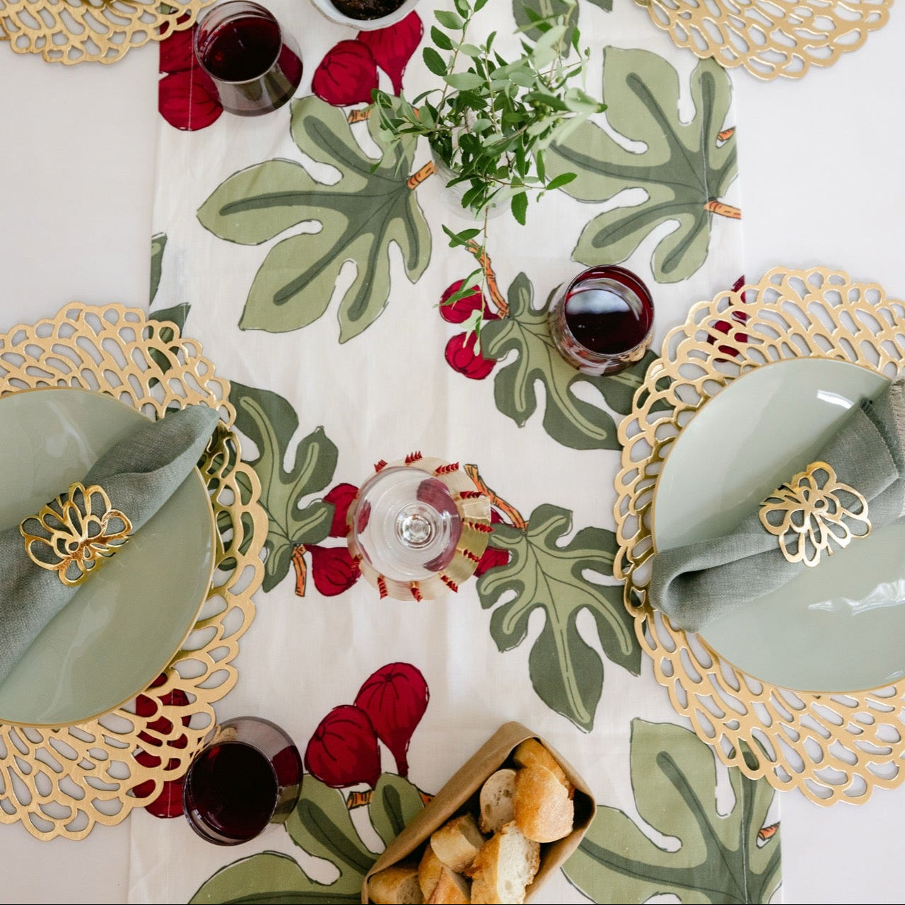 Decorative table setting with green leaf pattern, gold rimmed plates, and red accents.