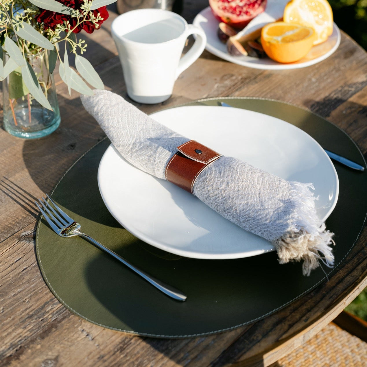 Table setting with a plate, fork, napkin, and coffee on a wooden table outdoors.