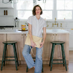 Person standing in a kitchen with wooden cabinets and green stools.