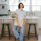 Person standing in a kitchen with wooden cabinets and green stools.