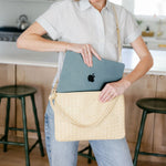 Woman holding a beige handbag with an Apple laptop inside in a kitchen.