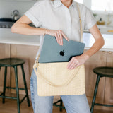 Woman holding a beige handbag with an Apple laptop inside in a kitchen.