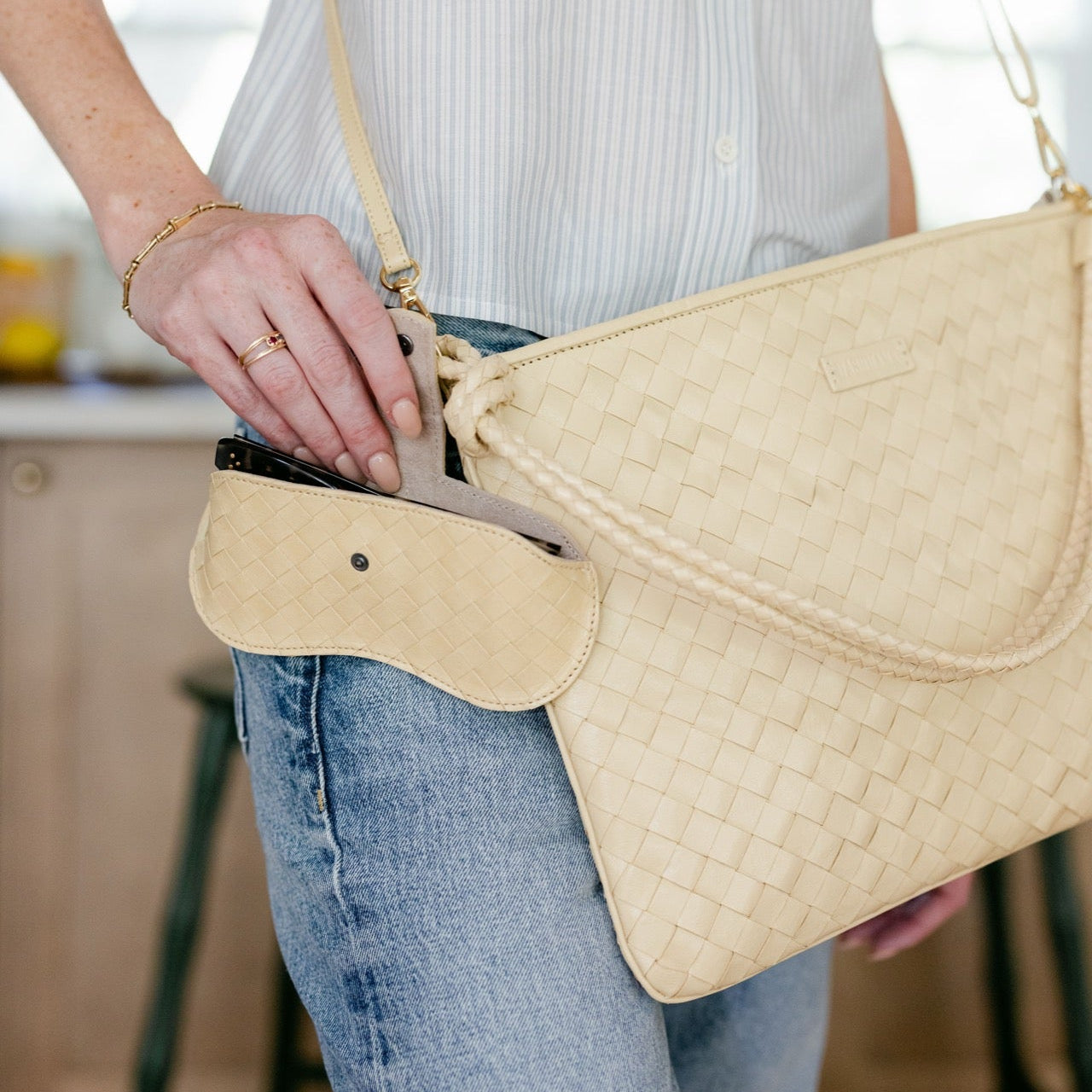 Person holding a beige woven handbag in an indoor setting