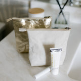Gold and white makeup bag with a tube of cream on a light surface