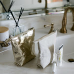 Gold and silver makeup bags on a bathroom counter with a tube of cream.