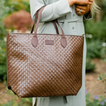 Person holding a brown woven handbag with a blurred natural background