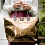 Person holding a large brown tote bag with leather handles.