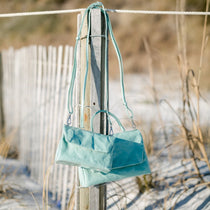 Turquoise handbag hanging on a wooden post with a beach background