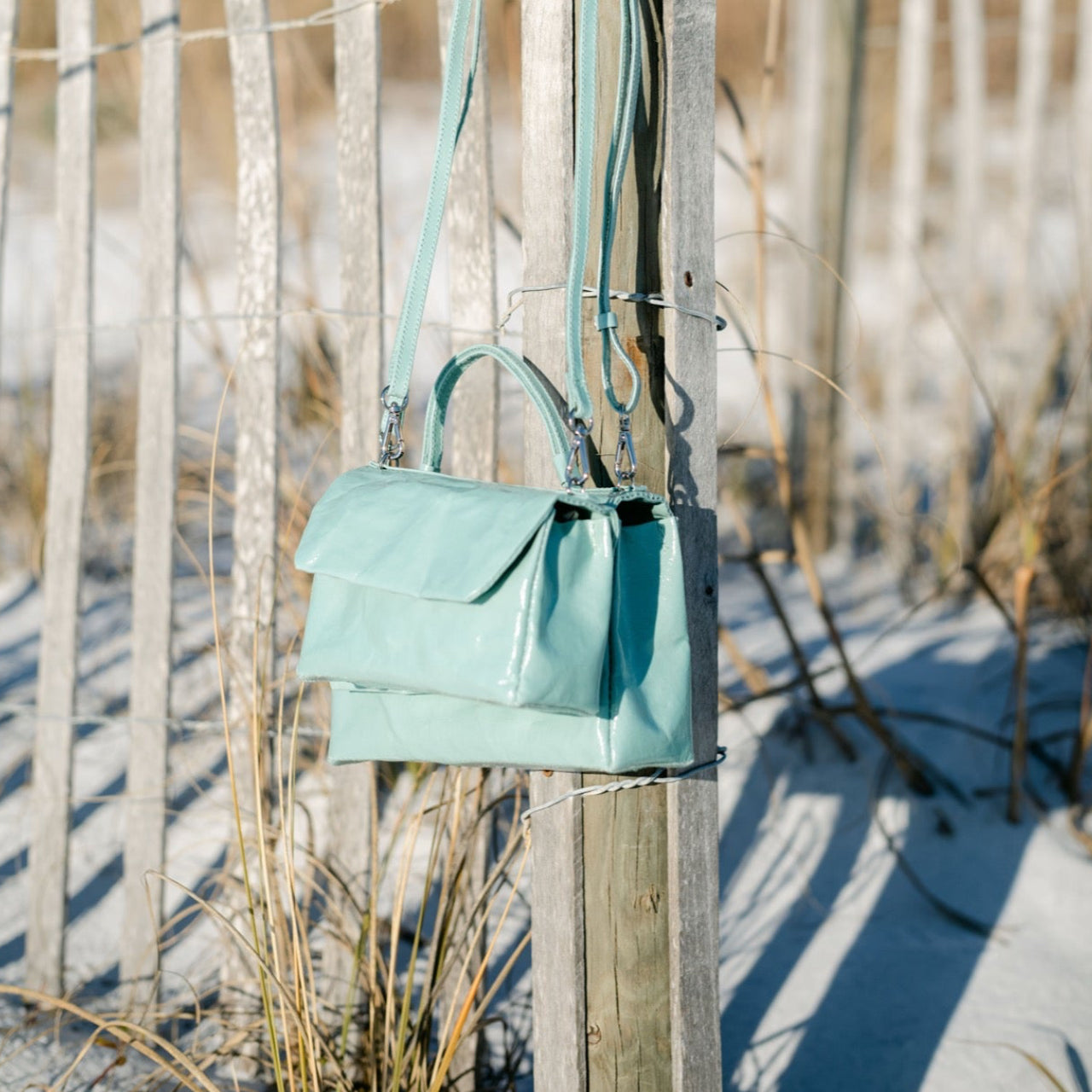 Light blue handbag hanging on a wooden post with a beach background