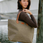 Woman holding an olive tote handbag with brown leather handles