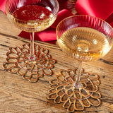 Two gold-rimmed cocktail glasses with red liquid on decorative coasters with a red floral background.
