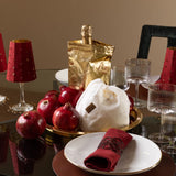 Dining table setting with red napkins, pomegranates, and a gold bag on a reflective surface.