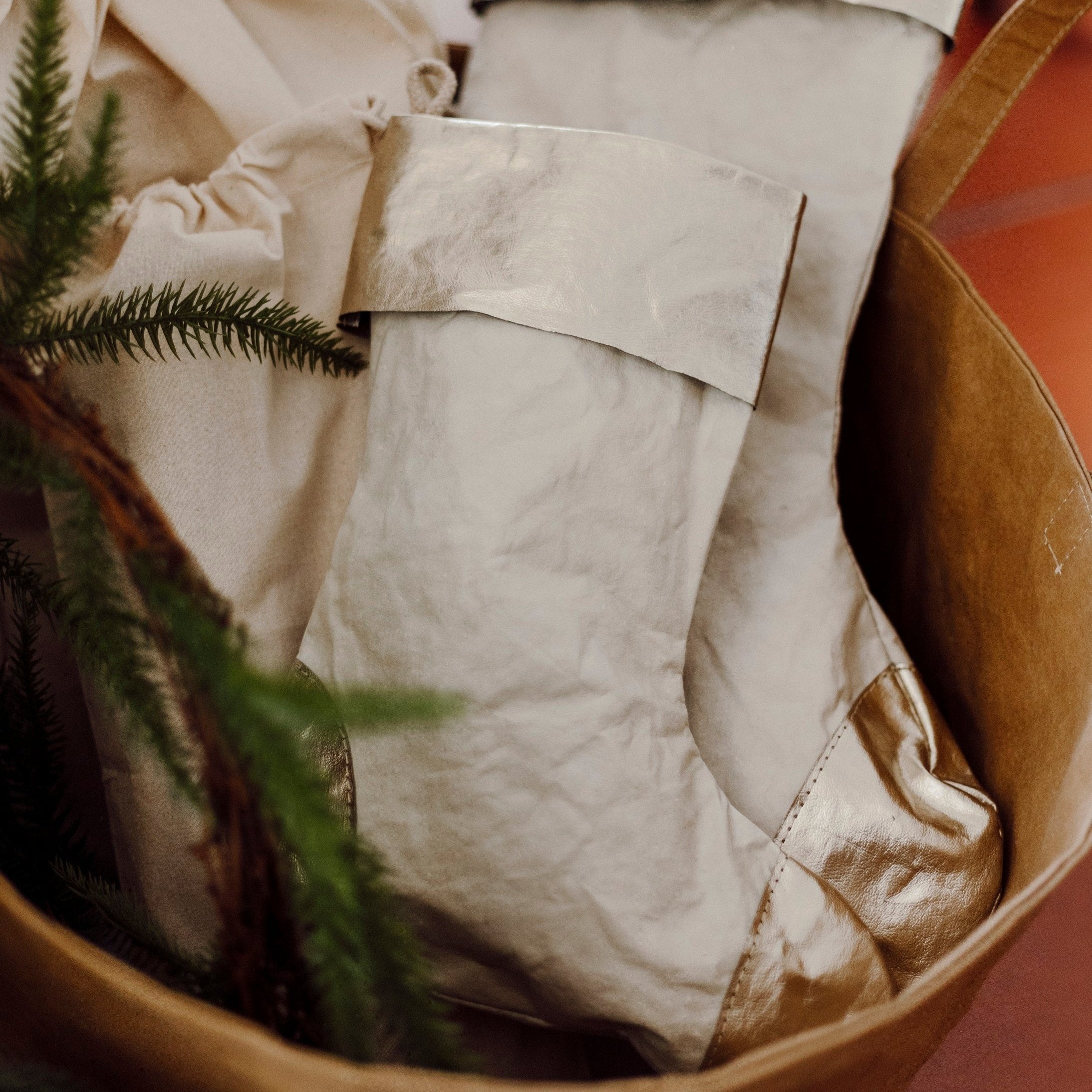 A tan washable paper basket is shown holding two washable paper Christmas stockings, one large and one small. The stockings are pale cream in colour with a platinum metallic cuff, heel and toe.