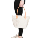 Person holding a white tote bag with brown handles on a white background