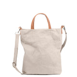 A washable paper tote bag is shown from the front angle. It has a relaxed shape, two top handles and a long shoulder strap. It is pale grey in colour.