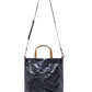 A washable paper tote is shown with a long shoulder strap pointing skywards. It has two top handles and is metallic navy in colour.