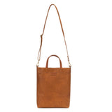 A washable paper tote is shown with a long shoulder strap pointing skywards. It has two top handles and is rich tan in colour.