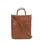 A woven washable paper tote bag is shown from the front angle. It features two top handles and a long adjustable shoulder strap. It is brown in colour.