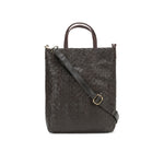 A woven washable paper tote bag is shown from the front angle. It features two top handles and a long adjustable shoulder strap. It is chocolate brown in colour.