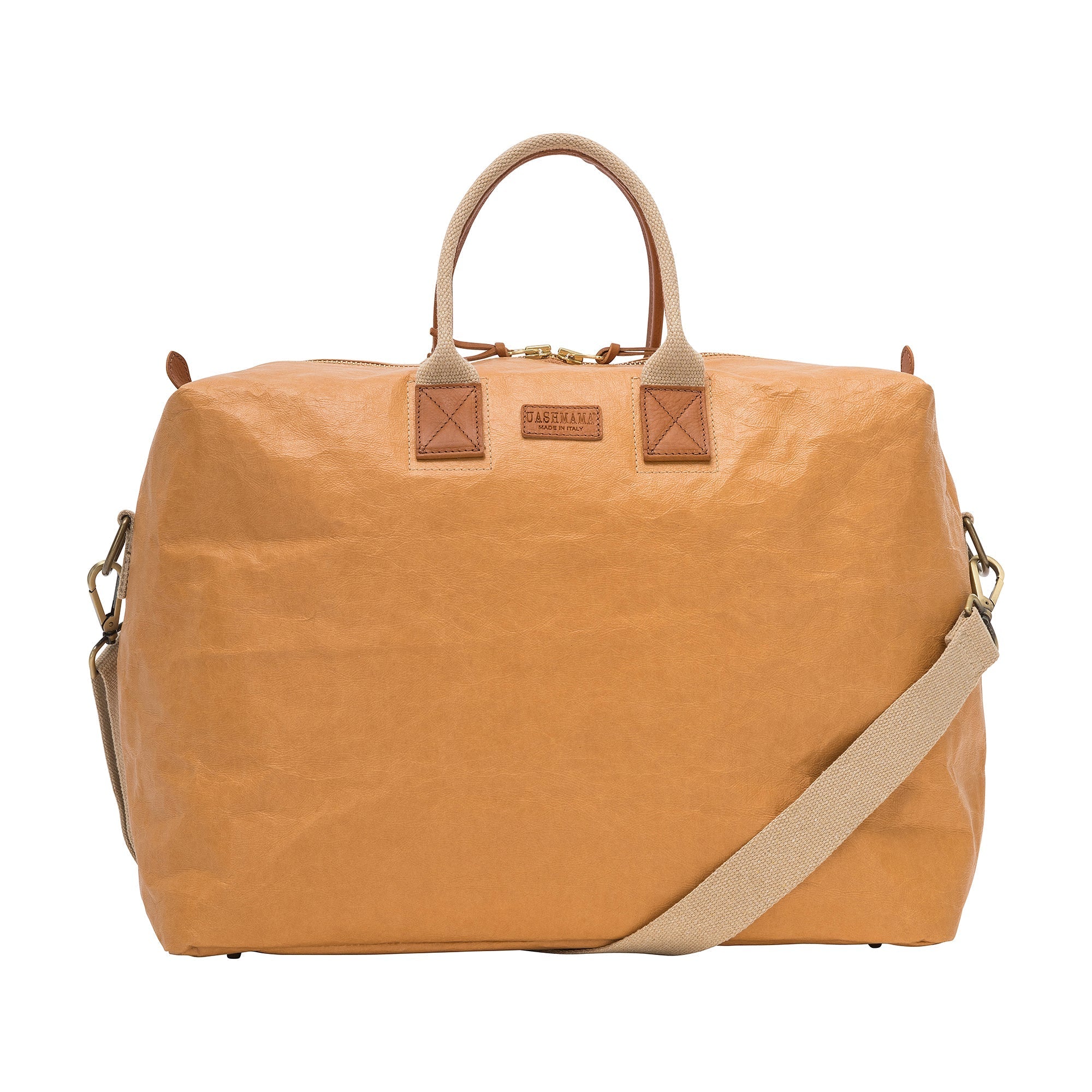 A washable paper holdall with two short carry handles and one long fabric strap. The holdall closes with a zip which has leather zip pulls. The holdall has leather details attaching the straps to the bag and a small UASHMAMA leather logo label. The bag shown is tan with tan leather details. The holdall is extra large in size.