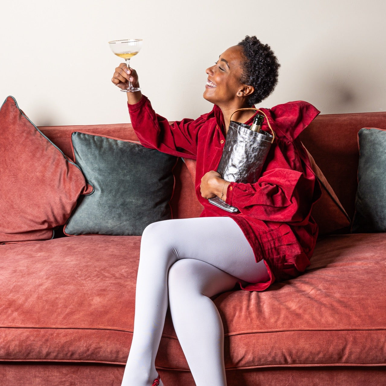 Woman in a red outfit sitting on a couch holding a glass of wine.
