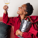 Person in a red outfit holding a cocktail and a metallic bag on a couch.