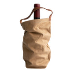 A red wine bottle is shown inside a washable paper wine bag. The bag has a small brown leather handle at the top for carrying. The washable paper wine bag shown is light tan.