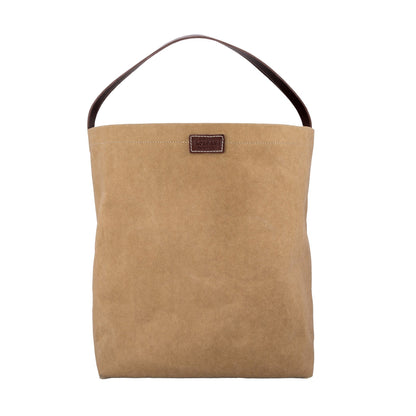 A tan washable paper handbag is shown from the front. It features a singular top handle in chocolate brown, and a brown UASHMAMA logo stamp on the front.
