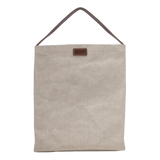 A cream washable paper handbag is shown from the front. It features a singular top handle in chocolate brown, and a brown UASHMAMA logo stamp on the front.