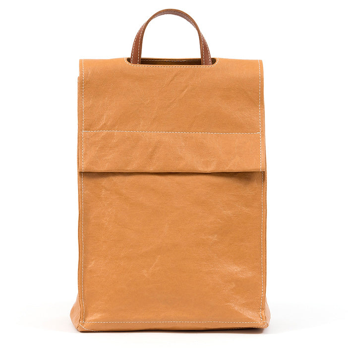 A tall rectangular square-edged washable paper backpack with a front flap and a brown top handle is shown in a natural tan colour, with white stitching.