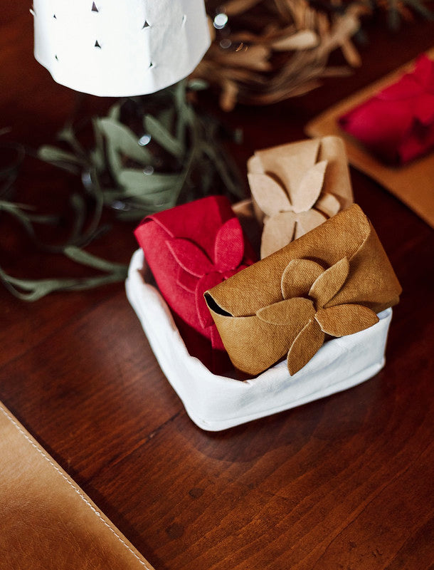 Three washable paper gift cards are shown wrapped in a washable paper tie-handle pouch, inside a white washable paper tray. They are red, beige, and natural tan in colour.