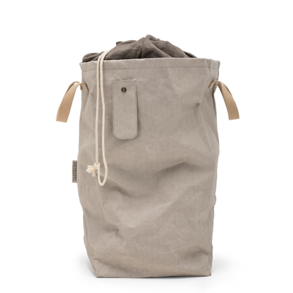 A washable paper laundry bag is shown in beige. It features two side handles, a popper tab, and an interior drawstring lining.