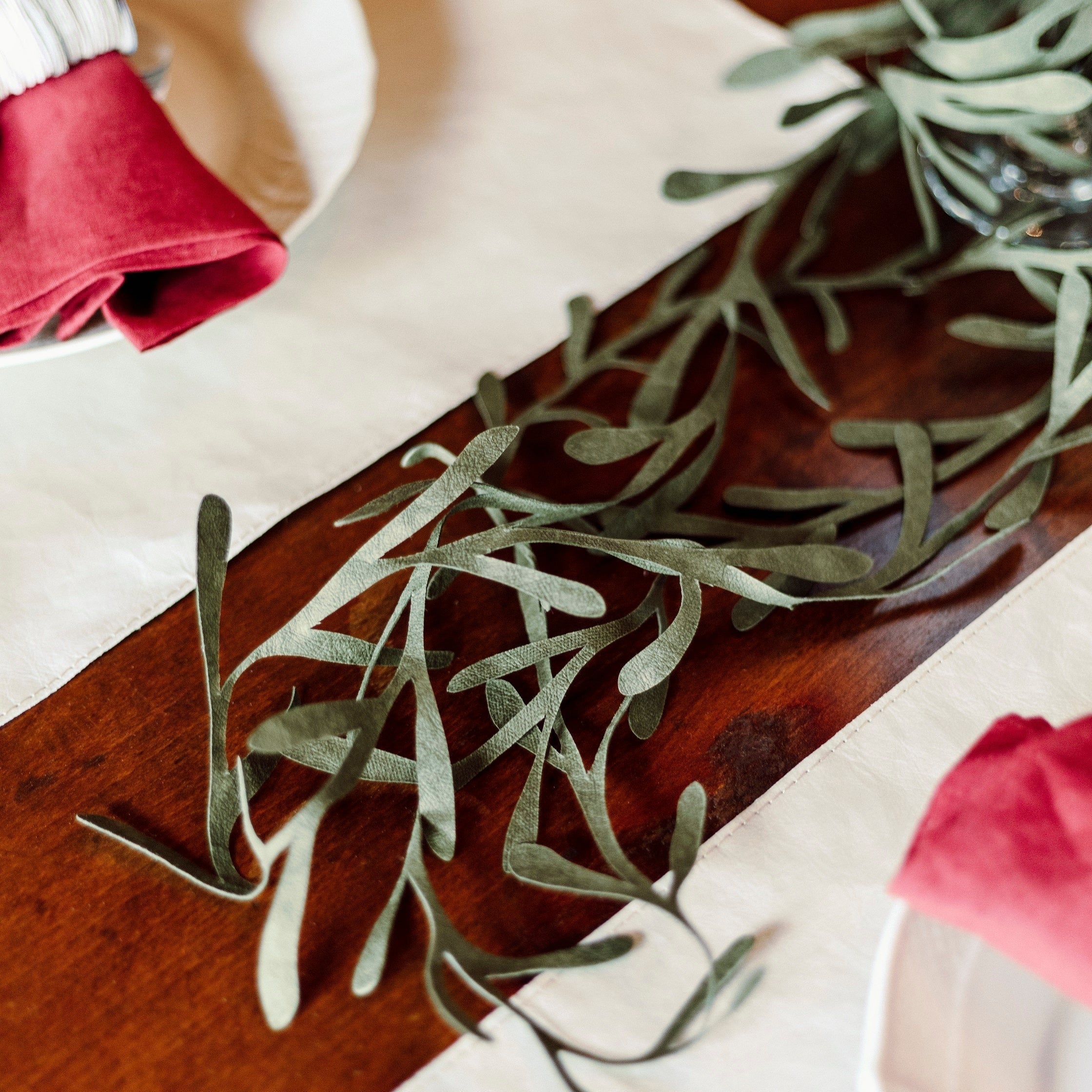 A green washable paper wreath is shown down the centre of a laid table.