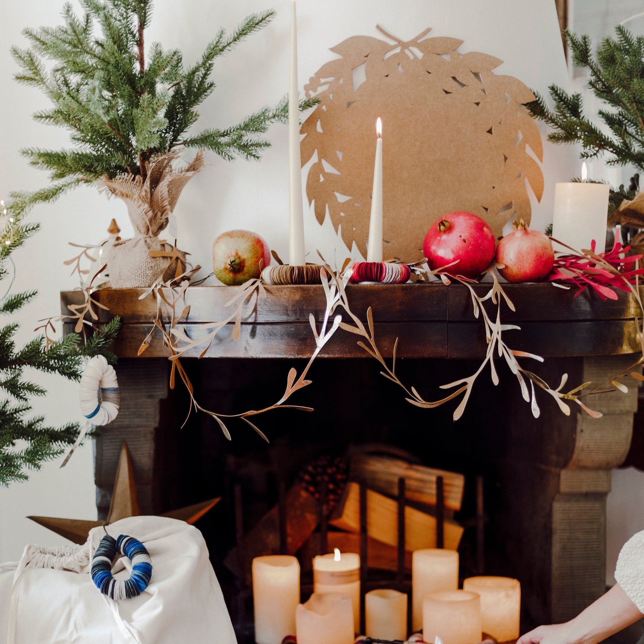 A gold washable paper wreath is shown adorning a mantlepiece in a Christmas setting. Washable paper totes, stockings, boxes and folios sit in the front of the image.