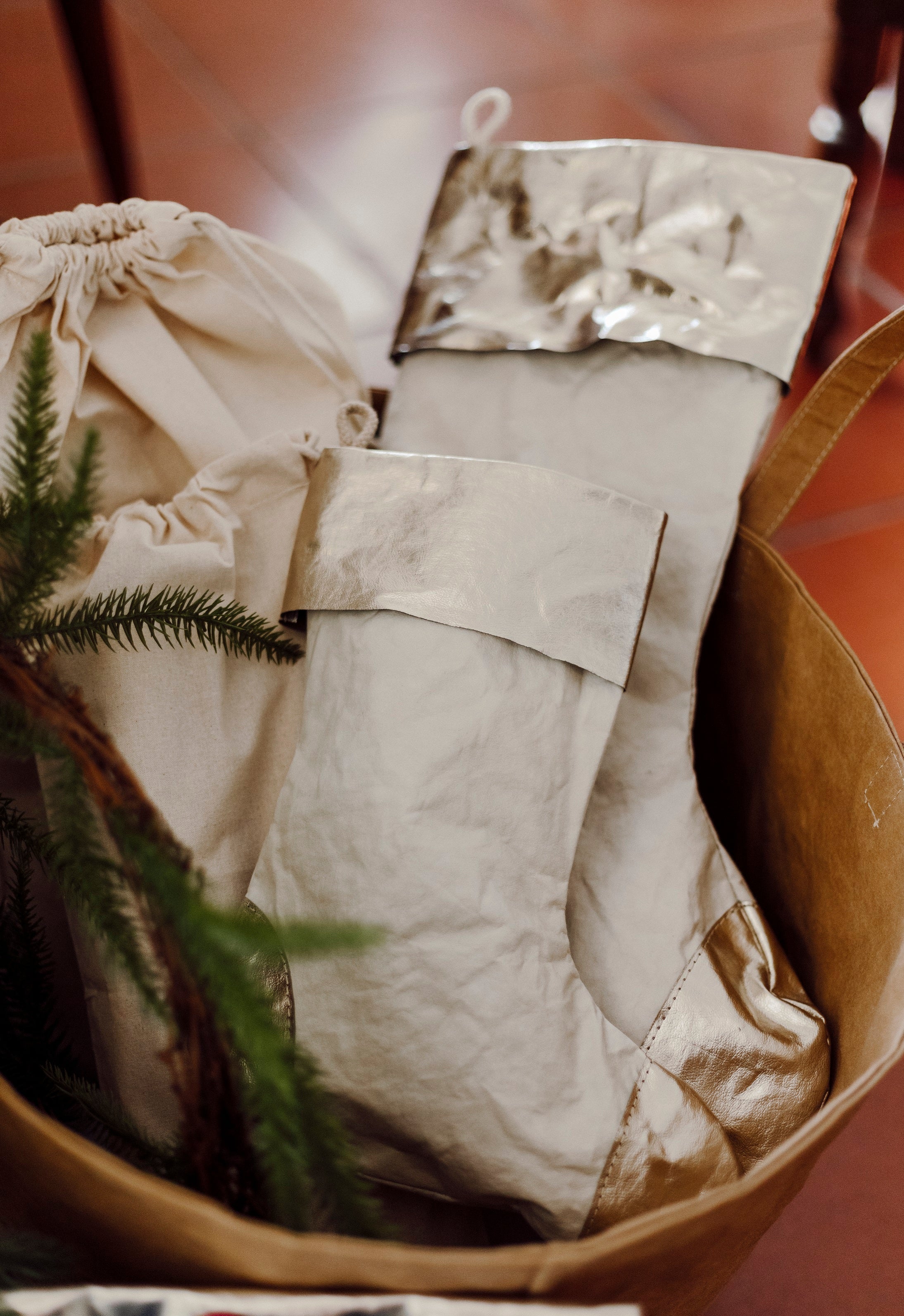 A tan washable paper basket is shown holding two washable paper Christmas stockings, one large and one small. The stockings are pale cream in colour with a platinum metallic cuff, heel and toe.