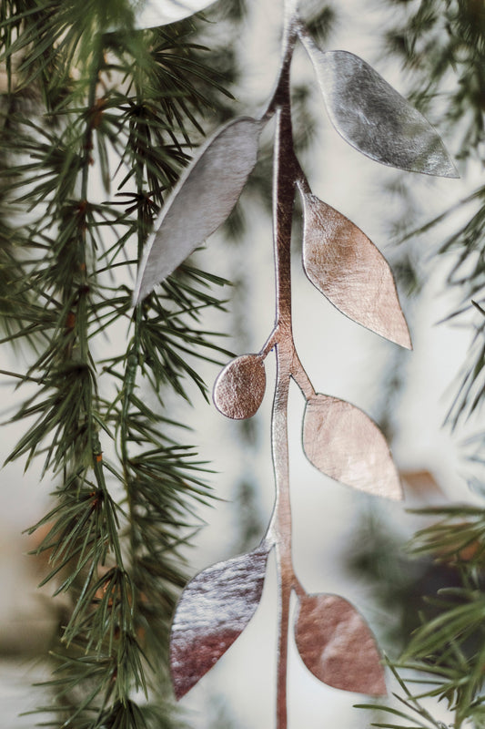 A washable paper garden wreath in metallic tones is shown dangling vertically from a Christmas tree.