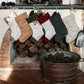 A stone fireplace is shown with six washable paper Christmas stockings hung in a row. In front of the fireplace is a metal bucket containing pine cones.