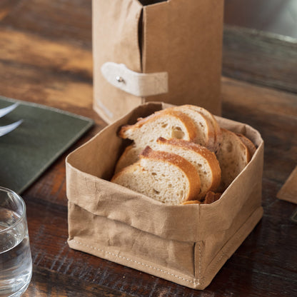 A washable paper tray in tan is shown containing sliced bread. A washable paper cooler in the same tone sits at rear.