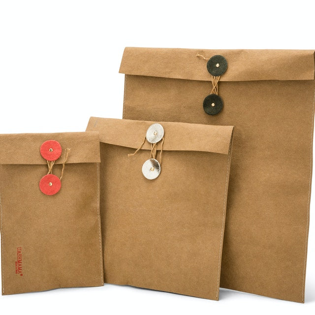 A set of three washable paper folio gift pouches are shown in varying sizes. They feature twine closures with round washable paper discs in red, gold and green respectively.