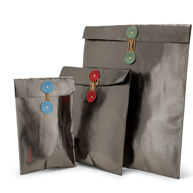 A set of pewter metallic washable paper gift pouches are shown in varying sizes. They are from left to right - small with blue closure, medium with red closure, and large with green closure.