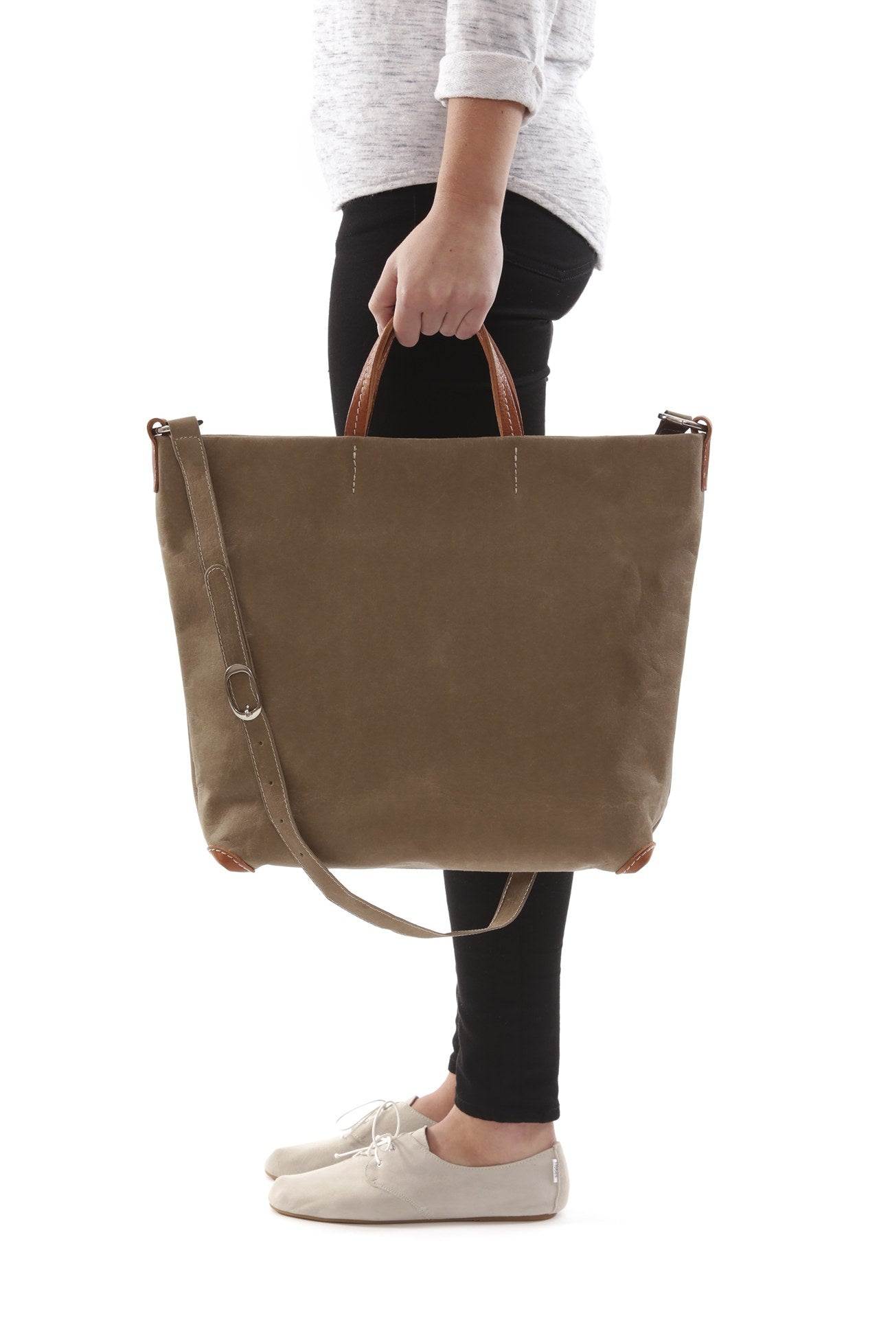 A woman is shown from a side view. She is carrying a sand coloured washable paper tote bag in her hand by the top handles.